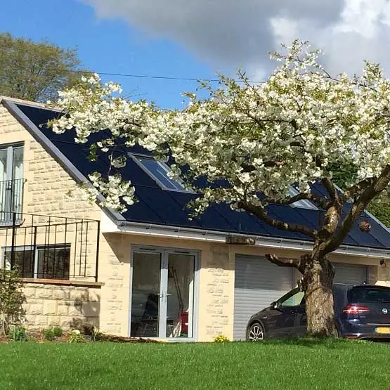 Solar panels on the roof of a stone house behind a flowering tree
