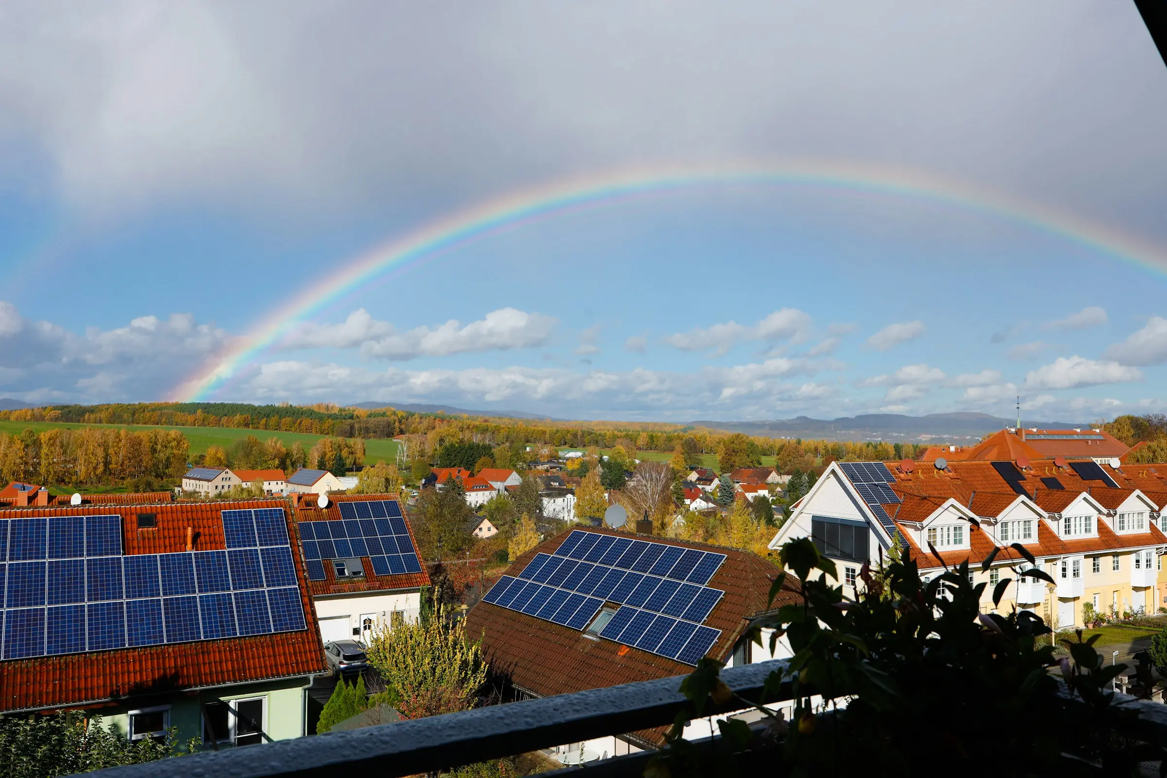 Houses with solar panels on their roofs under a rainbow